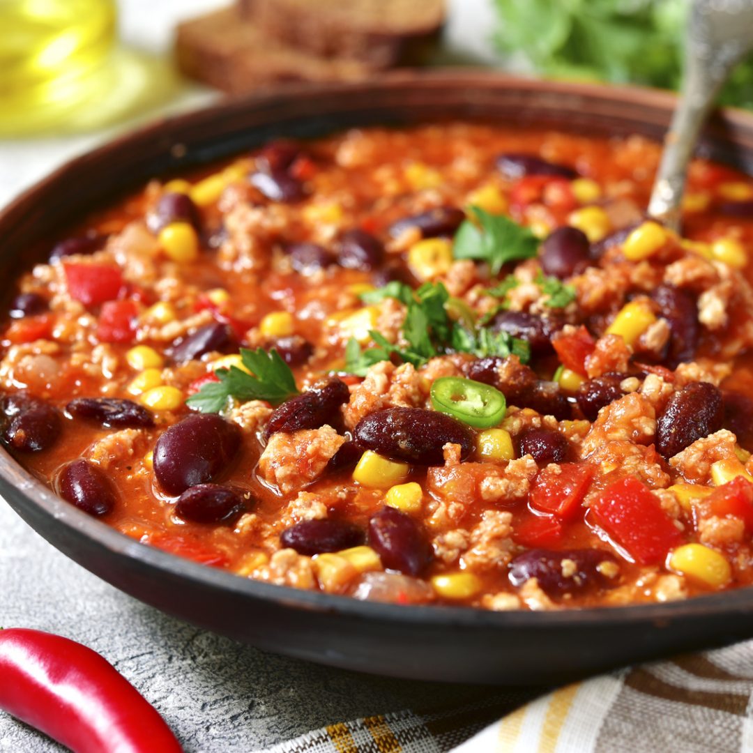 Chili con carne in a clay bowl on a concrete or stone background- traditional dish of mexican cuisine.